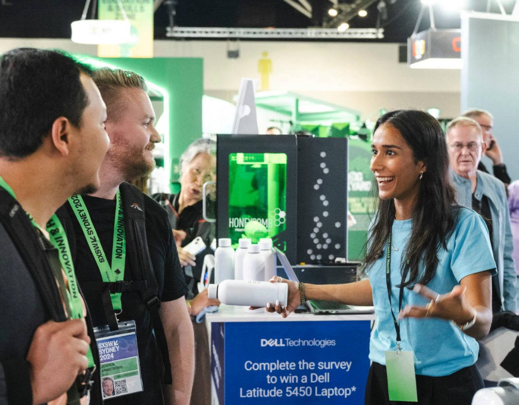 A MerchMovesUs representative talks with two attendees at a Dell Technologies trade-show booth.